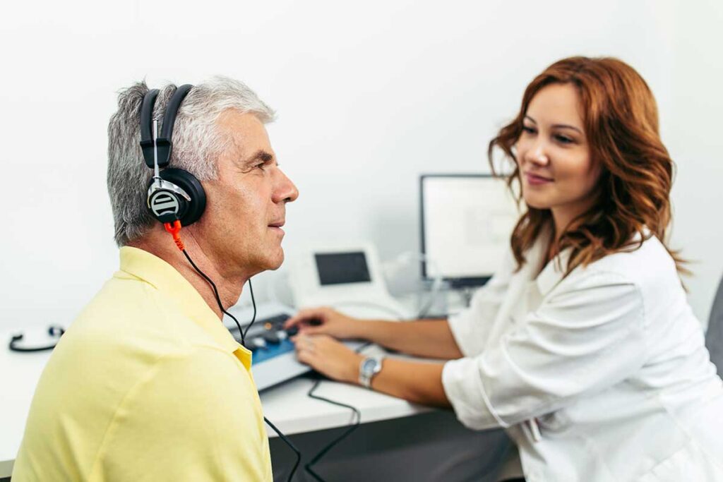 An audiologist showing an ear diagram to an adult patient in a bright, modern consultation room.