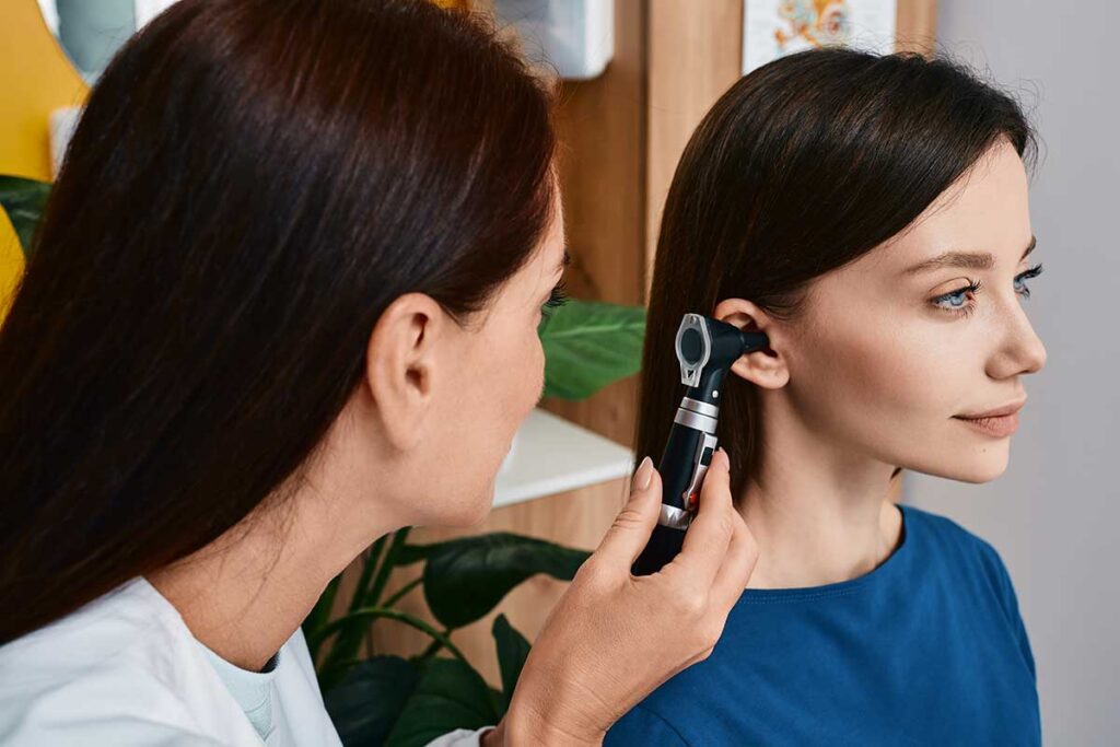 A middle-aged woman adjusting a discreet behind-the-ear hearing aid in a living room setting.