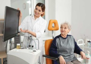 Person cleaning a hearing aid with a soft brush beside a dry storage case and charging station.